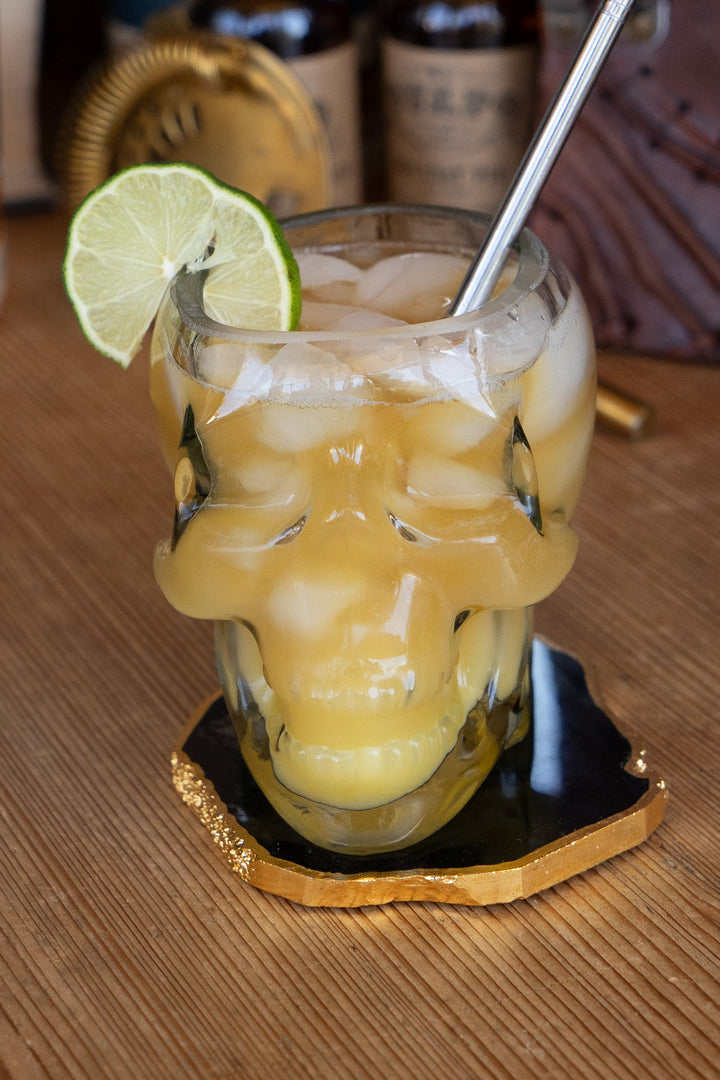 Skull whiskey glass with yellow drink, lime wedge, and metal straw
