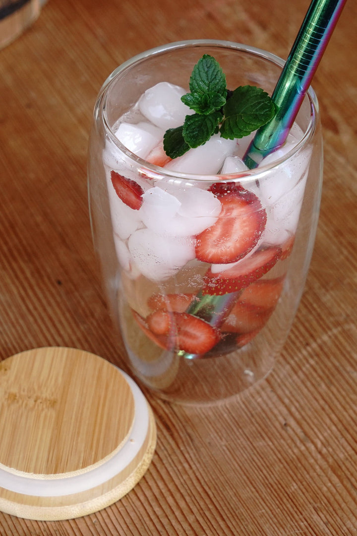 Double-walled glass mug with ice, strawberry slices, and mint; bamboo lid and seal ring.