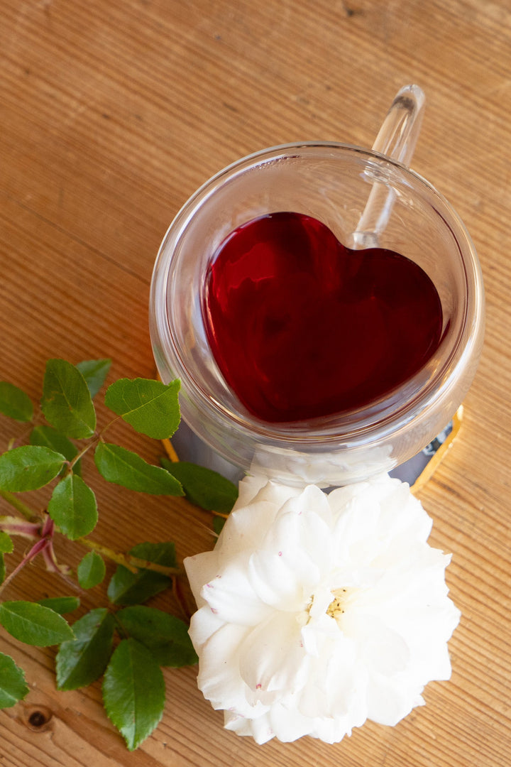 Clear double-walled glass mug filled with red tea, heart-shaped insert