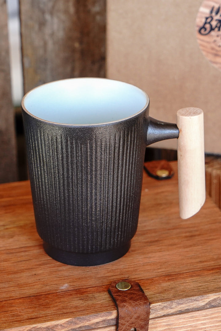Dark ribbed ceramic mug with light wood handle, mint-colored interior visible