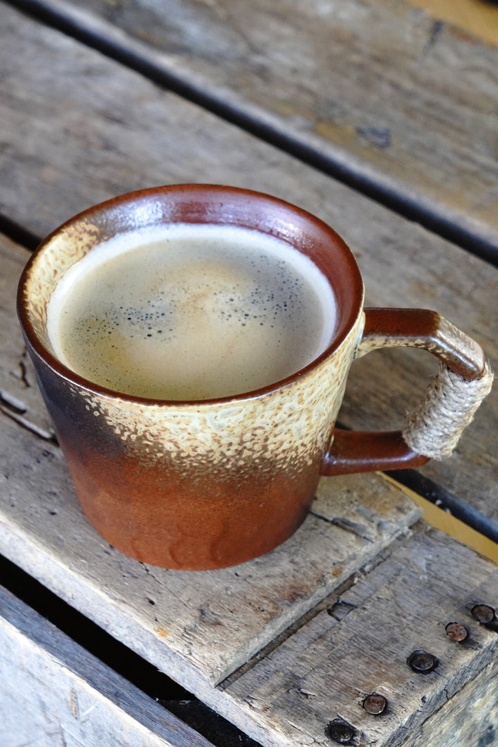 Stoneware coffee mug with speckled earth-toned glaze, filled interior, wrapped handle
