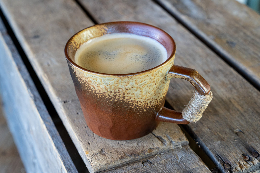 Brown and cream speckled ceramic coffee mug with wrapped handle on tabletop
