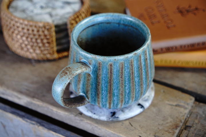 Handmade turquoise ceramic mug with vertical stripes and curved handle, speckled base