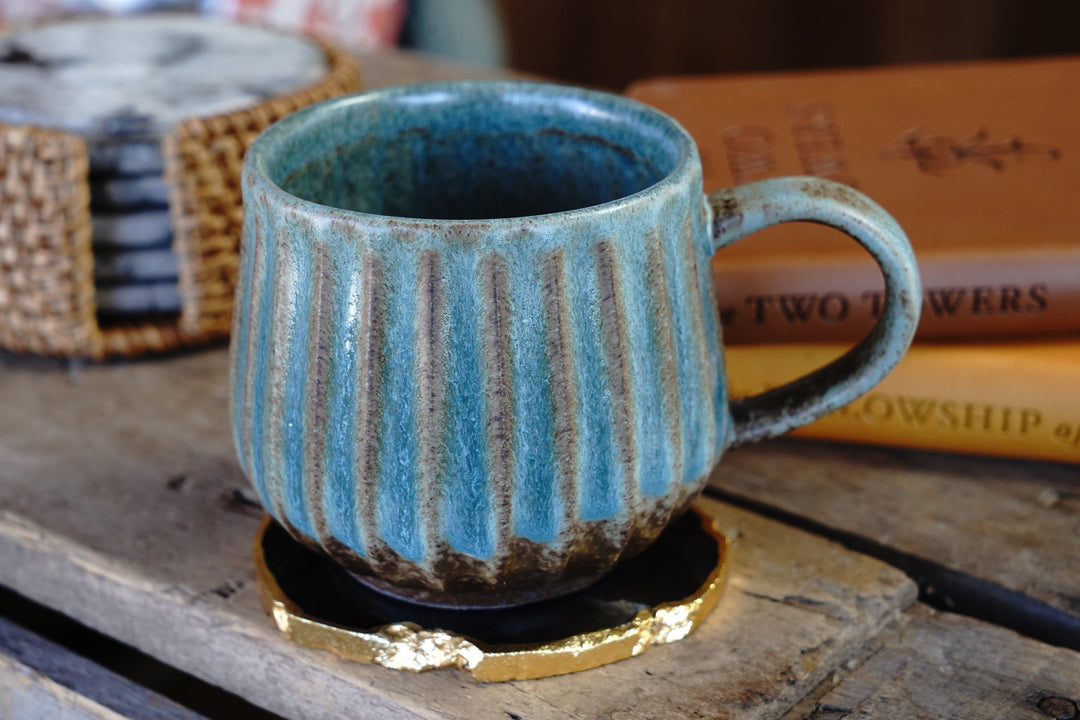 Handmade turquoise ceramic mug with vertical stripes, curved handle, dark interior