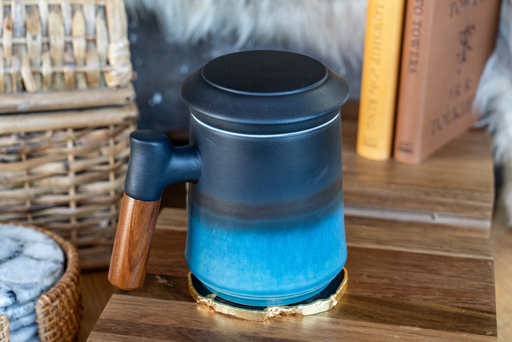 Blue ceramic tea mug with dark lid and wood handle, side view on table