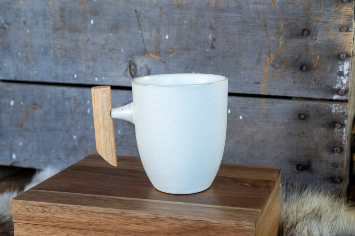 White ceramic mug with curved wooden handle, on a wooden display board