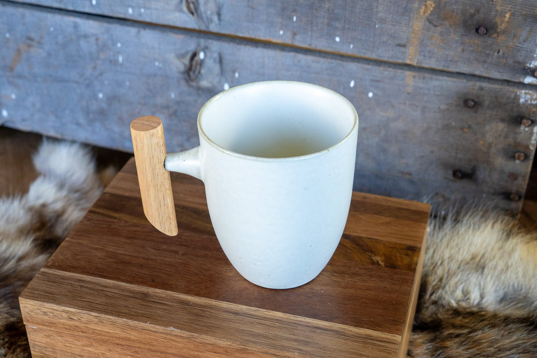 White ceramic mug with wooden handle, open top filled with light liquid
