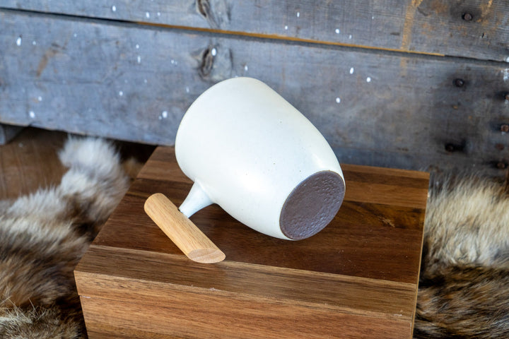 White ceramic mug with wooden handle, angled view showing base and rim