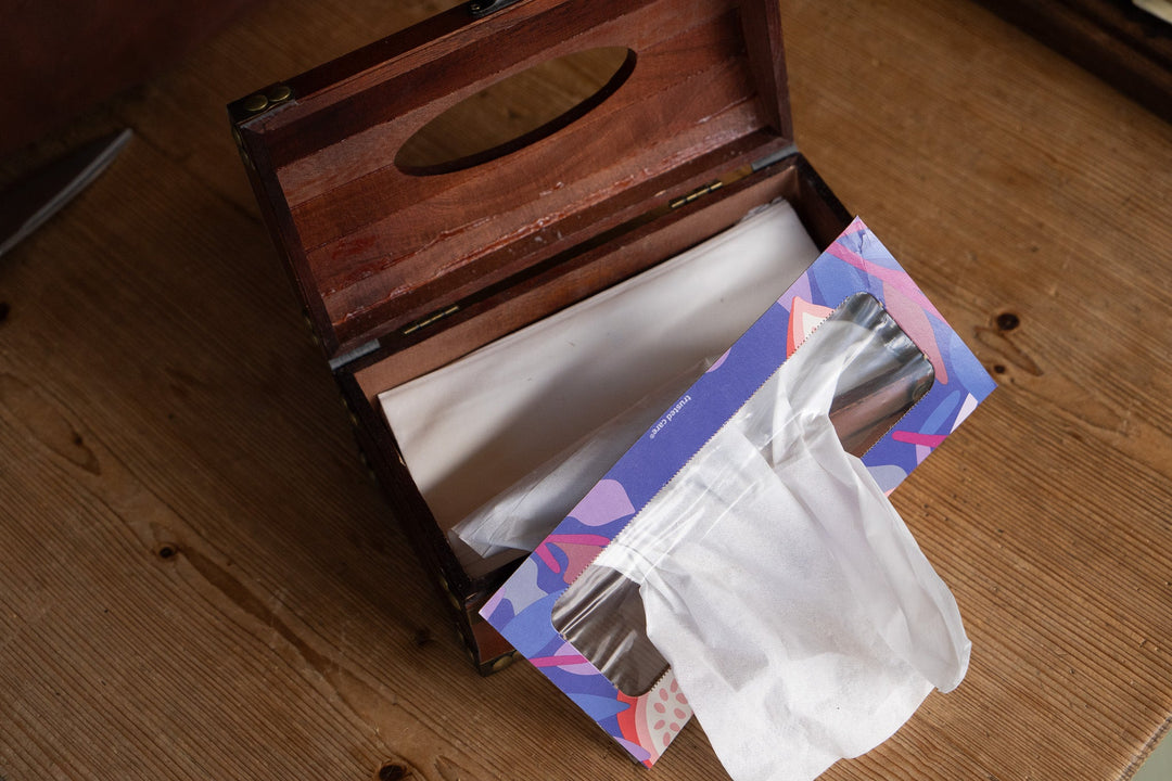 Cherry wooden tissue box with lid open on wooden floor, tissues and papers inside