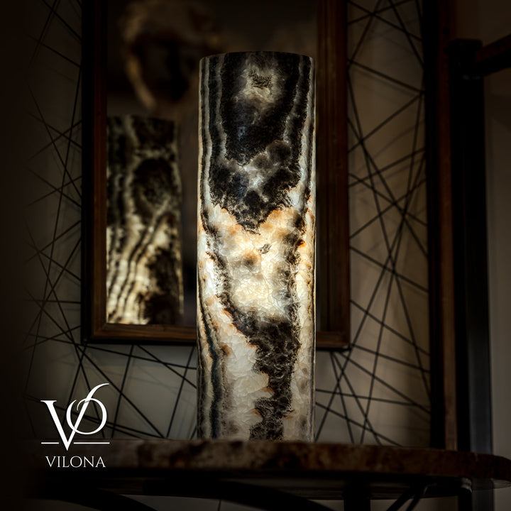 Onyx table lamp base centered on table, dark top and cream veining; cord trailing.