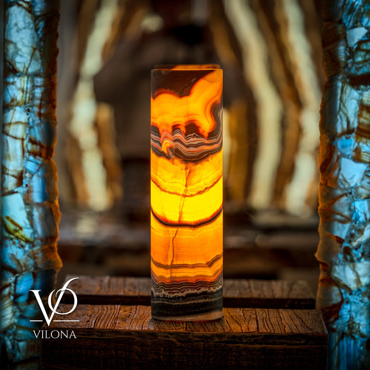 Onyx cylinder table lamp emitting warm orange light with layered mineral stripes