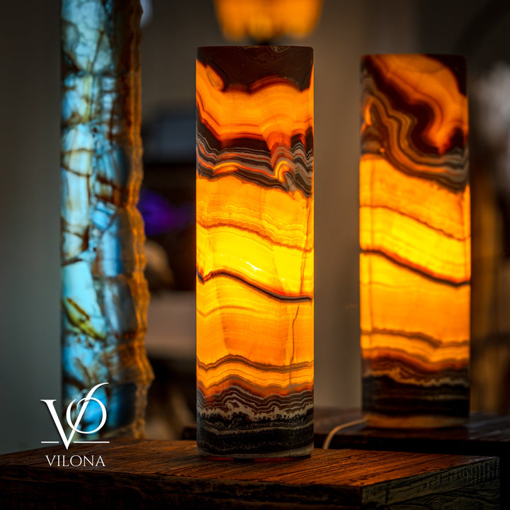Two onyx cylinder table lamps with vivid orange glow and dark horizontal stone bands