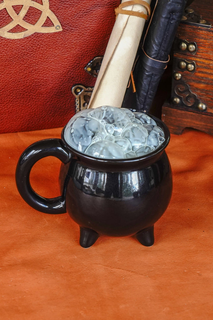 Black ceramic cauldron mug with side handle, filled with pale blue glowing ice.