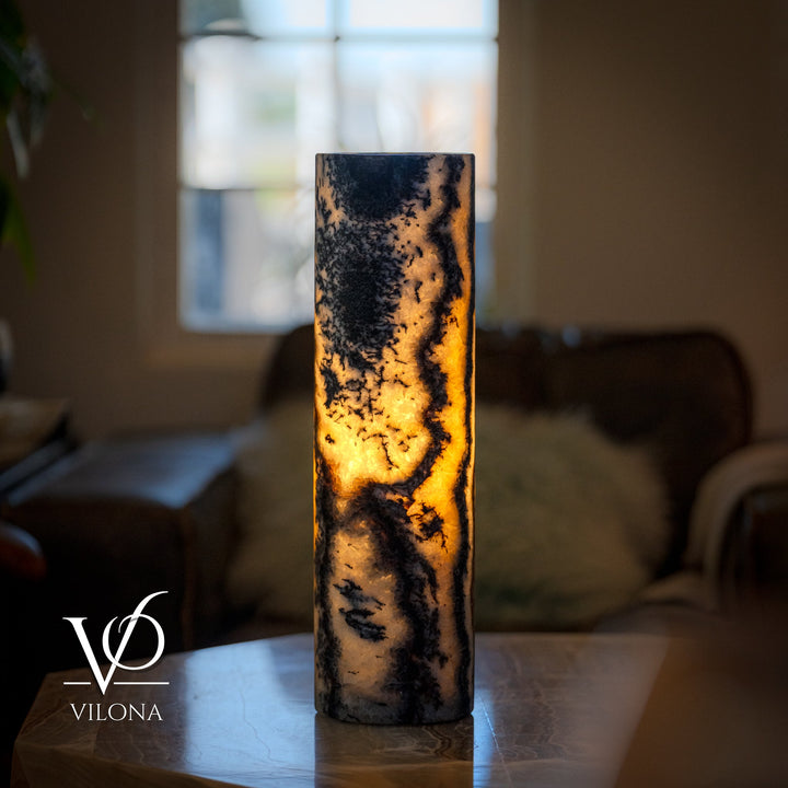 Onyx table lamp with tall cylindrical stone body, dark marbling, glowing warm light inside