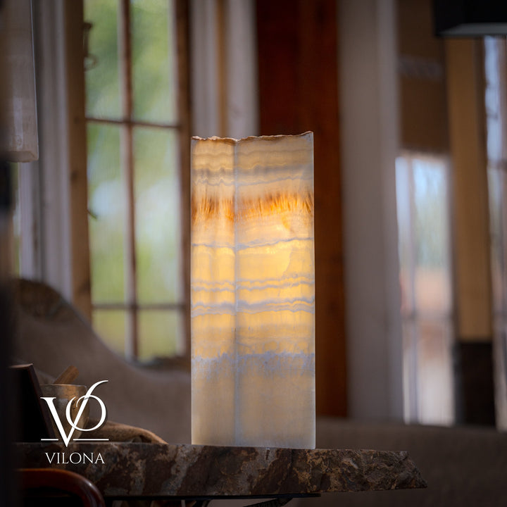 Square onyx table lamp with cream glowing shade and amber veining, centered on stone base