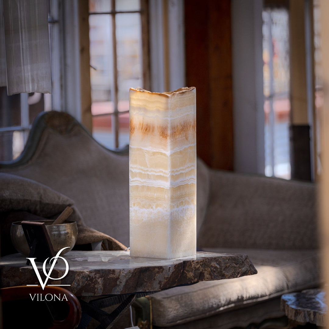 Square onyx table lamp with cream glass shade and amber streaks, lit on round stone slab