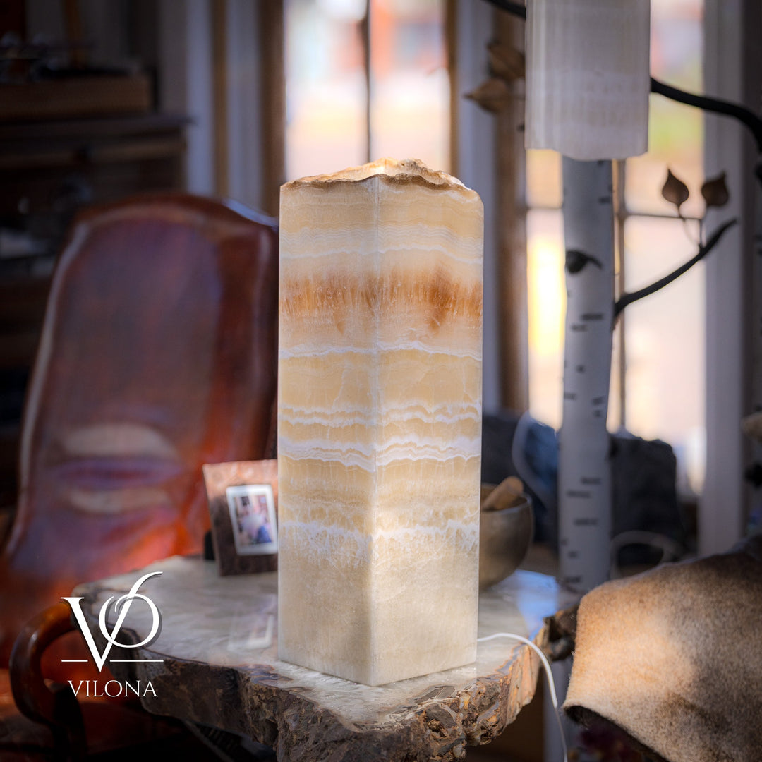 Square onyx table lamp with lit cream shade, amber veining, on rough stone base