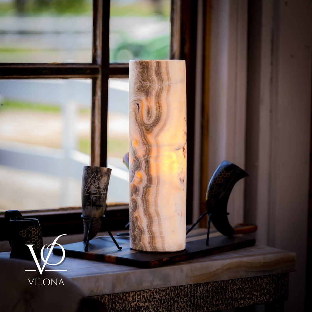 Cream cylindrical stone table lamp on a tabletop; vertical carved swirls with dark accents.