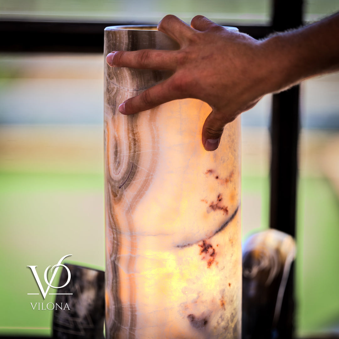 Close-up: hands gripping a cream cylindrical stone table lamp; swirling veins and marks visible.