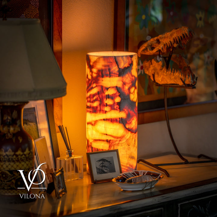 Table lamp with glowing amber marbled cylinder shade and dark metal base legs.
