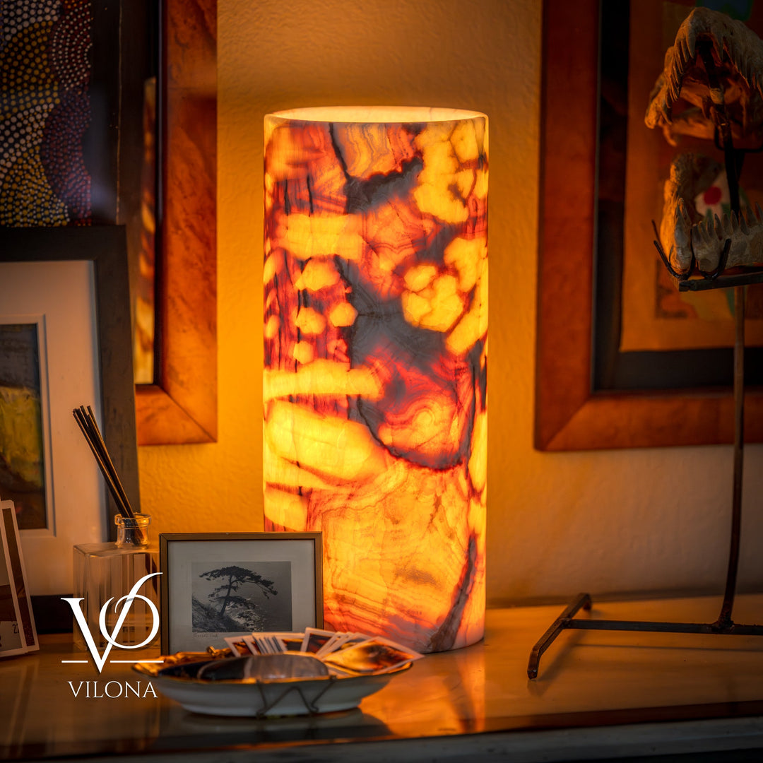 Table lamp with tall glowing amber marbled drum shade and dark base.