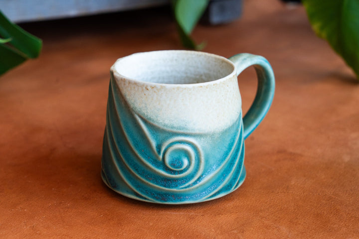 Ceramic wave mug with teal blue exterior, spiral swirl motif, and white interior