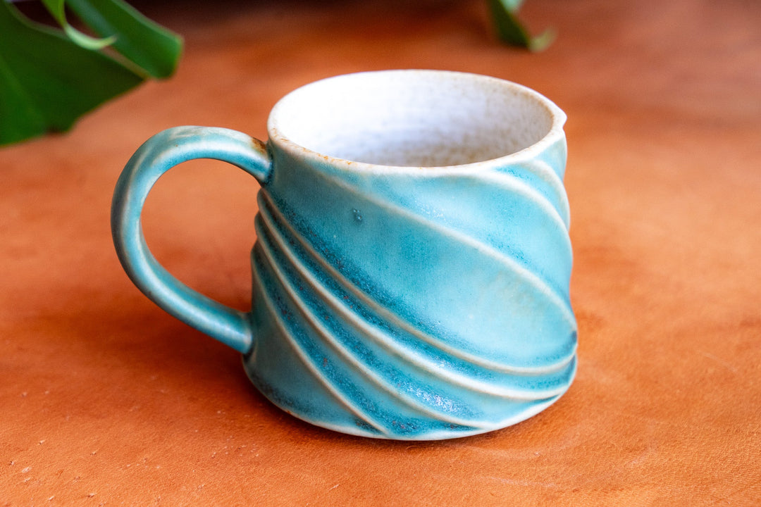 Teal ceramic wave mug with white interior rim and swirled stripe pattern