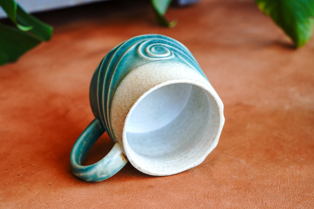 Ceramic mug with teal handle and wave glaze; open top with white interior
