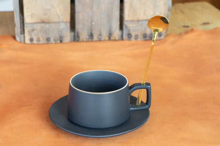 Matte blue bistro mug with saucer and gold spoon on tabletop