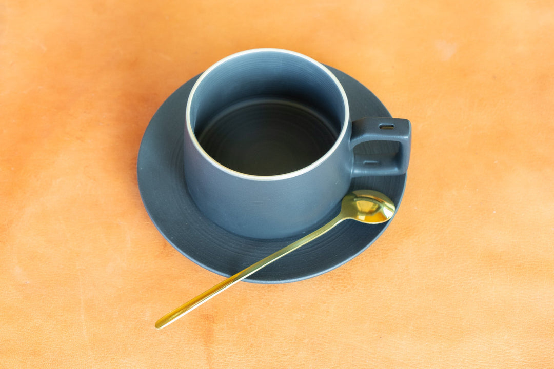 Matte blue bistro mug with saucer and gold spoon on tabletop