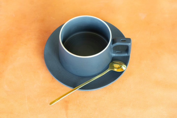 Matte blue bistro mug with saucer and gold spoon on tabletop