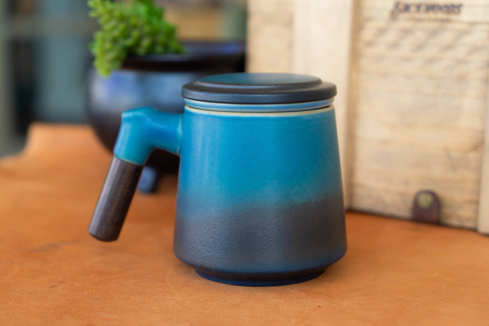 Blue ceramic tea steeping mug with lid and short side handle, angled view