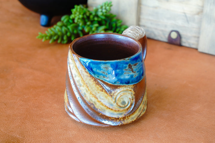 Rustic ceramic mug with blue interior, wave design, and rope-wrapped handle