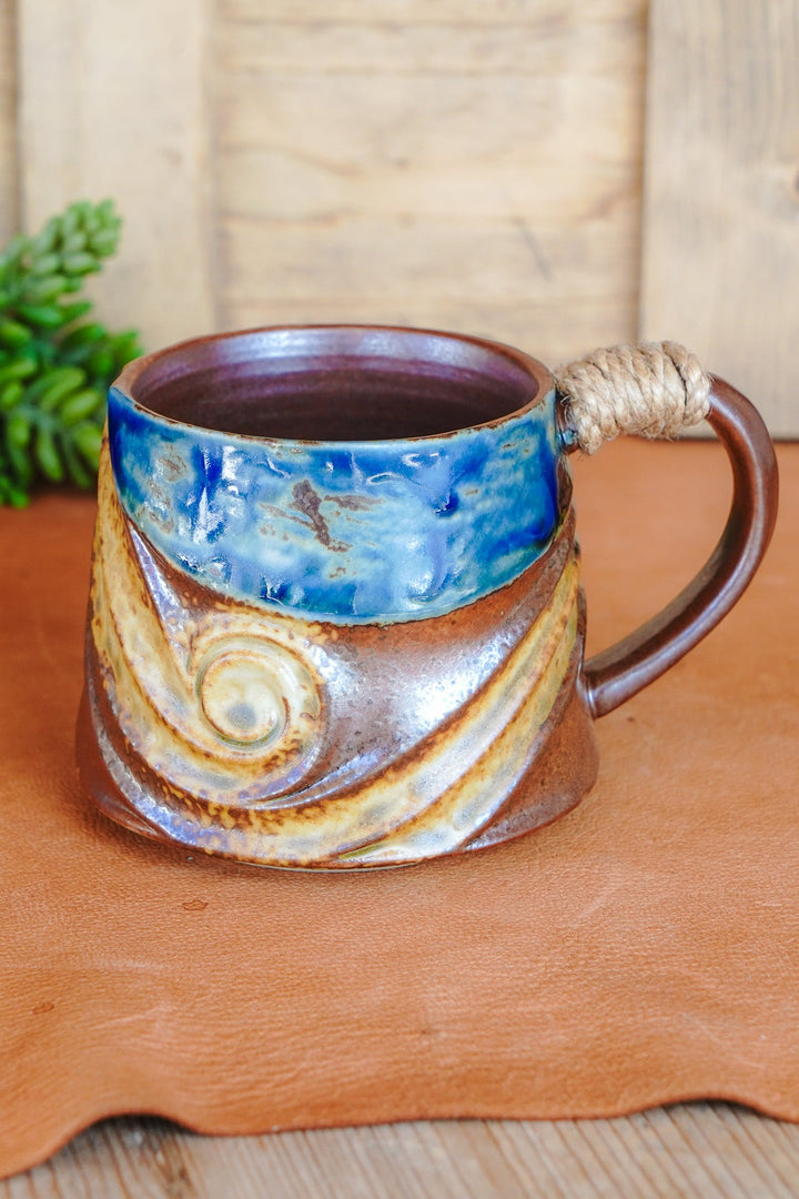 Rustic ceramic mug with blue rim, brown body, and rope-wrapped handle