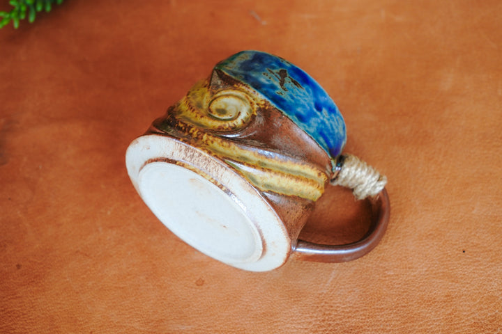 Bottom of rustic ceramic mug with blue-and-brown wave design and rope handle
