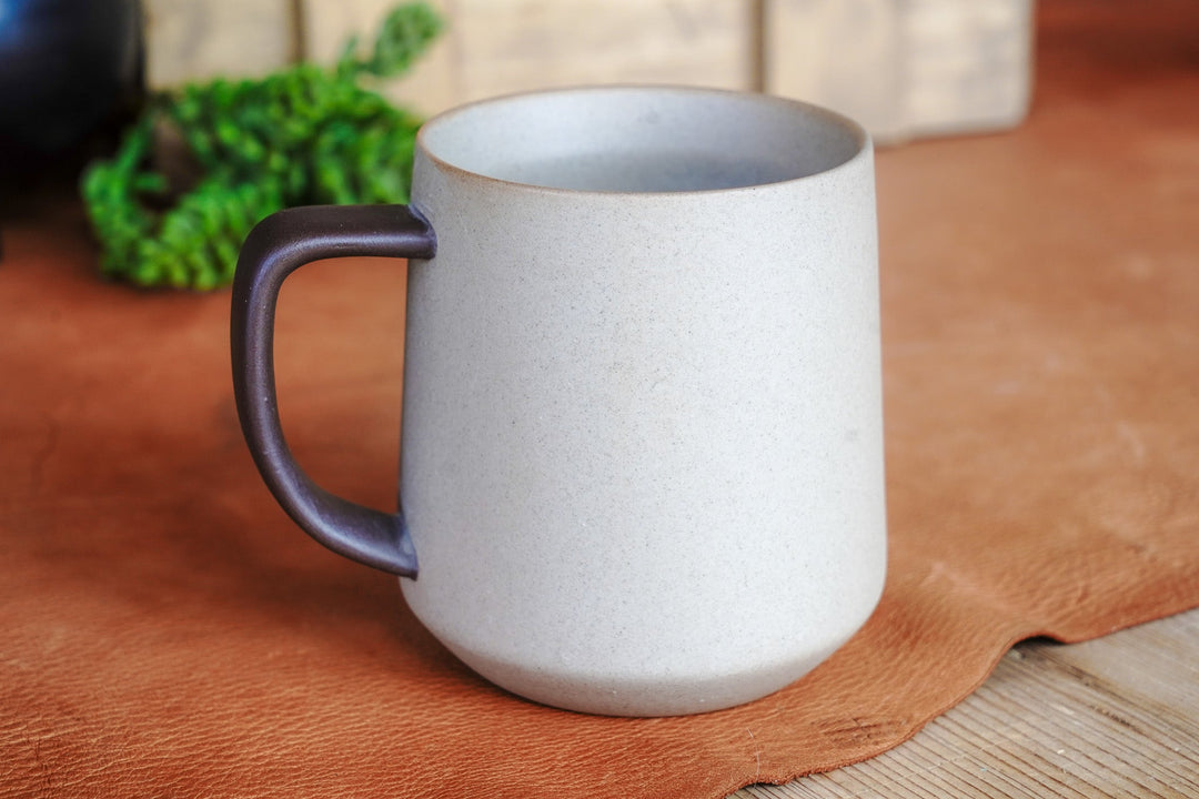 Two-tone ceramic mug on tabletop with dark handle and rim, speckled light body