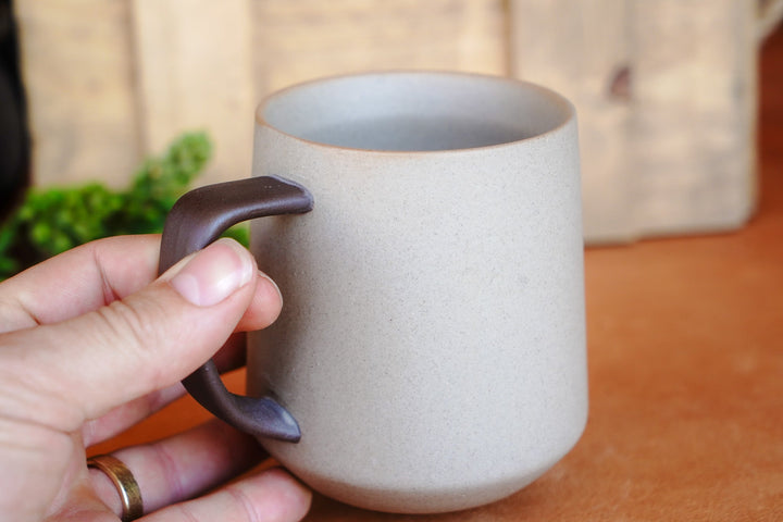 Ceramic mug with dark handle, light speckled body; hand holding the handle