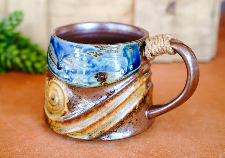 Rustic ceramic mug with blue top, wave pattern, and rope-wrapped handle