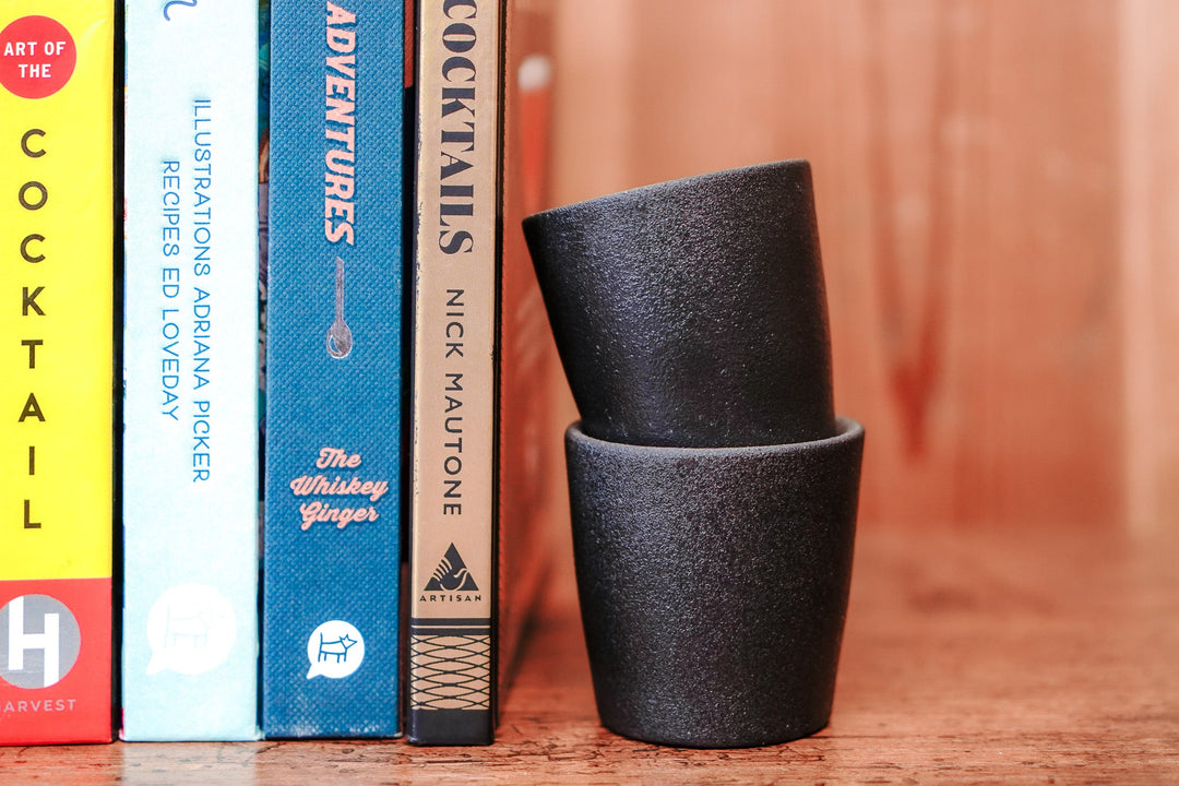 Two stacked matte stoneware shot glasses with dark, speckled texture