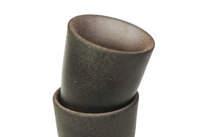 Stacked matte stoneware shot glass with dark textured surface and wide opening