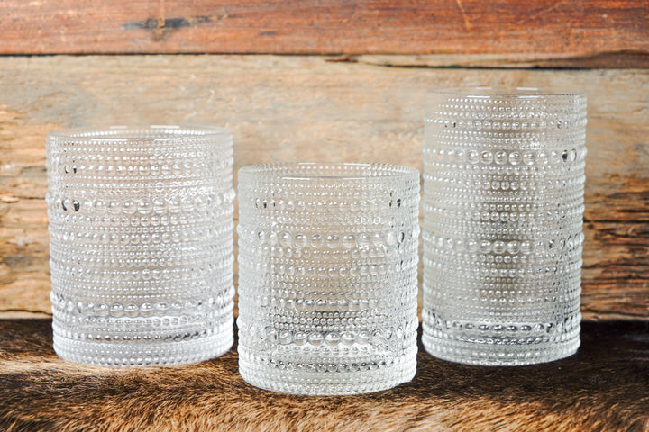Three clear bubbled glass tumbler cups with raised bead pattern, stacked on wood surface