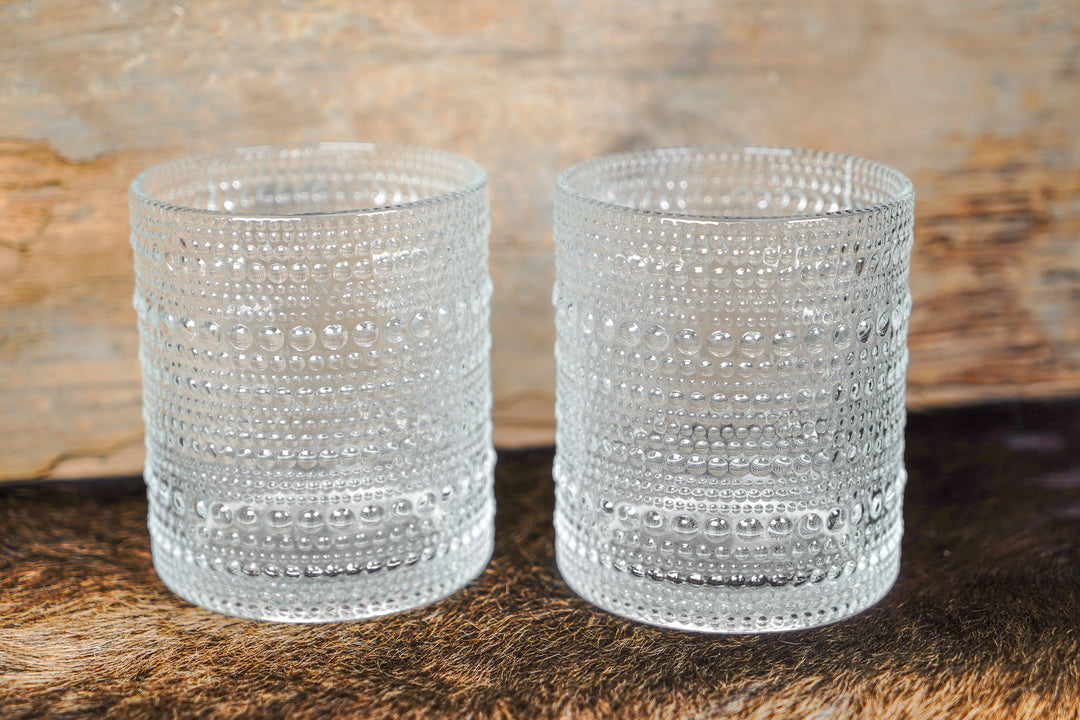 Two clear bubbled glass cylinder cups with raised bead pattern and stacked banded rows