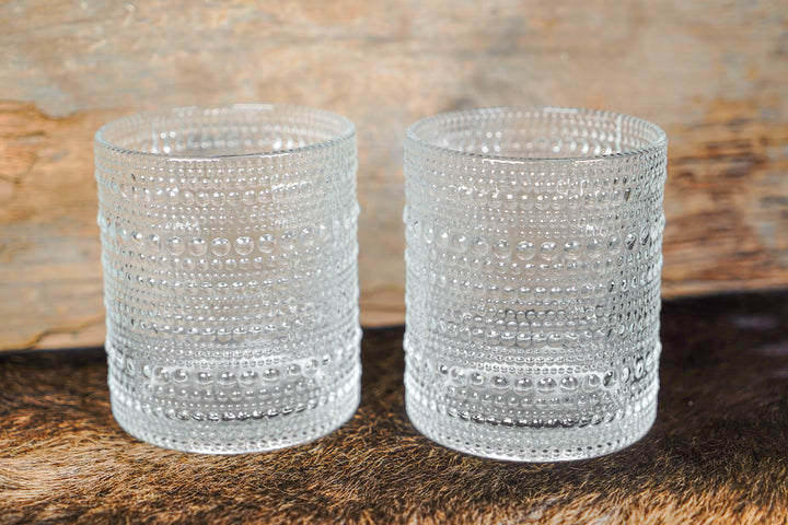 Two clear bubbled glass cylinder cups with raised bead pattern and stacked banded rows