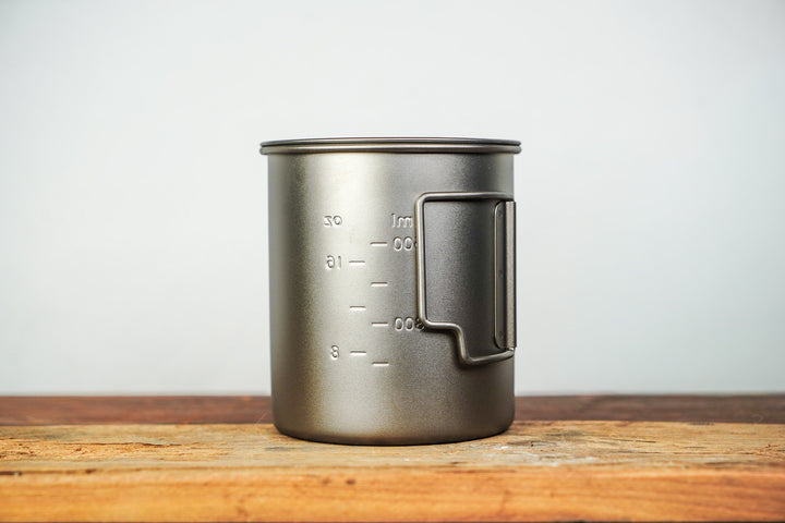 Metal camp cup with lid and side handle, volume measurement markings on the body