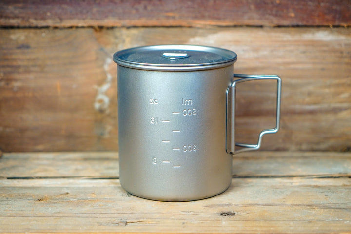 Dark metal camp cup with lid and side handle, with volume measurement markings