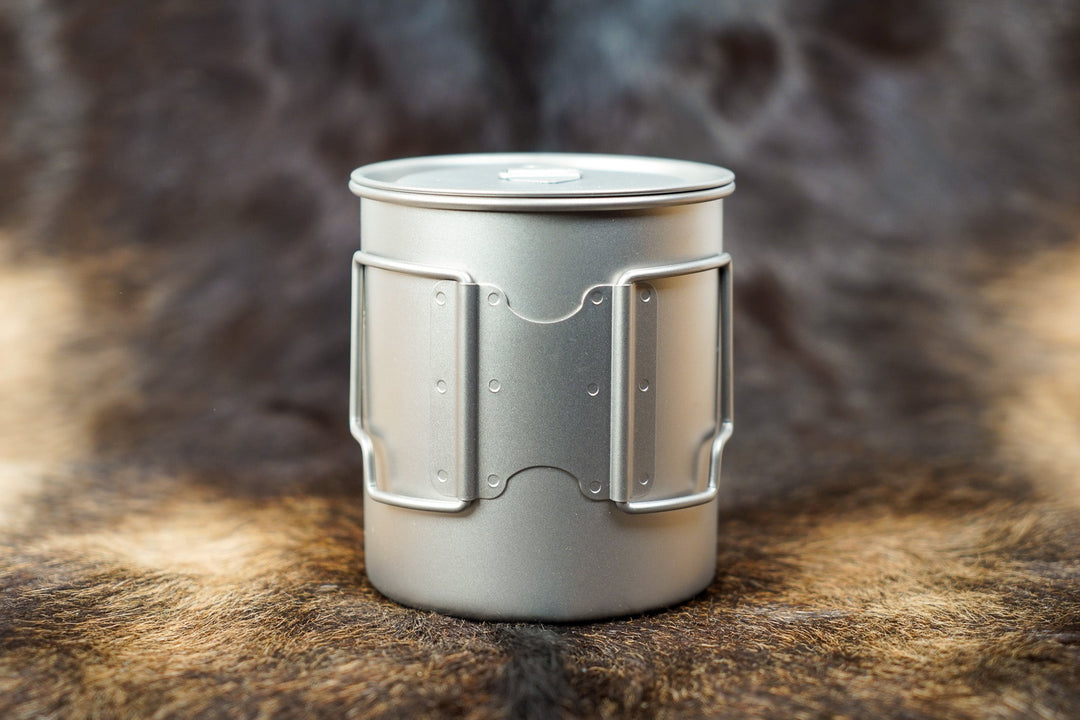 Light-colored On The Trail camp cup with lid and side handles, metal measuring marks