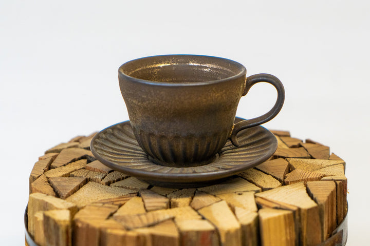 Brown speckled espresso cup with wide handle on ribbed saucer, stacked on wood chips