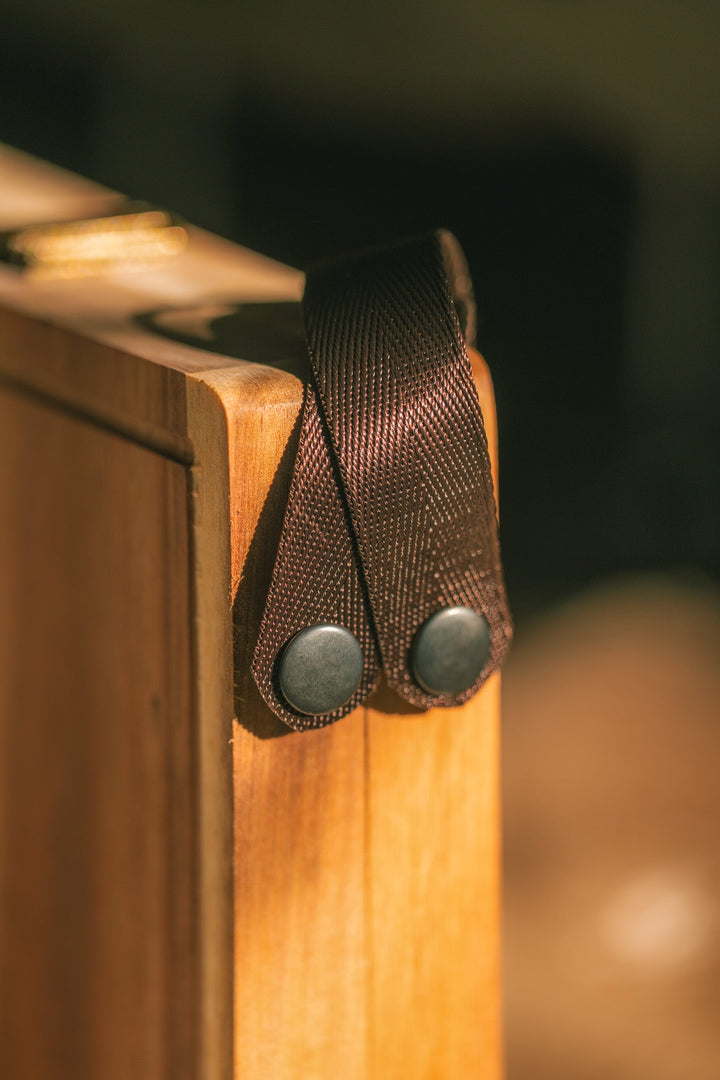 Dark webbing handle attached to a wooden folding cheese board corner