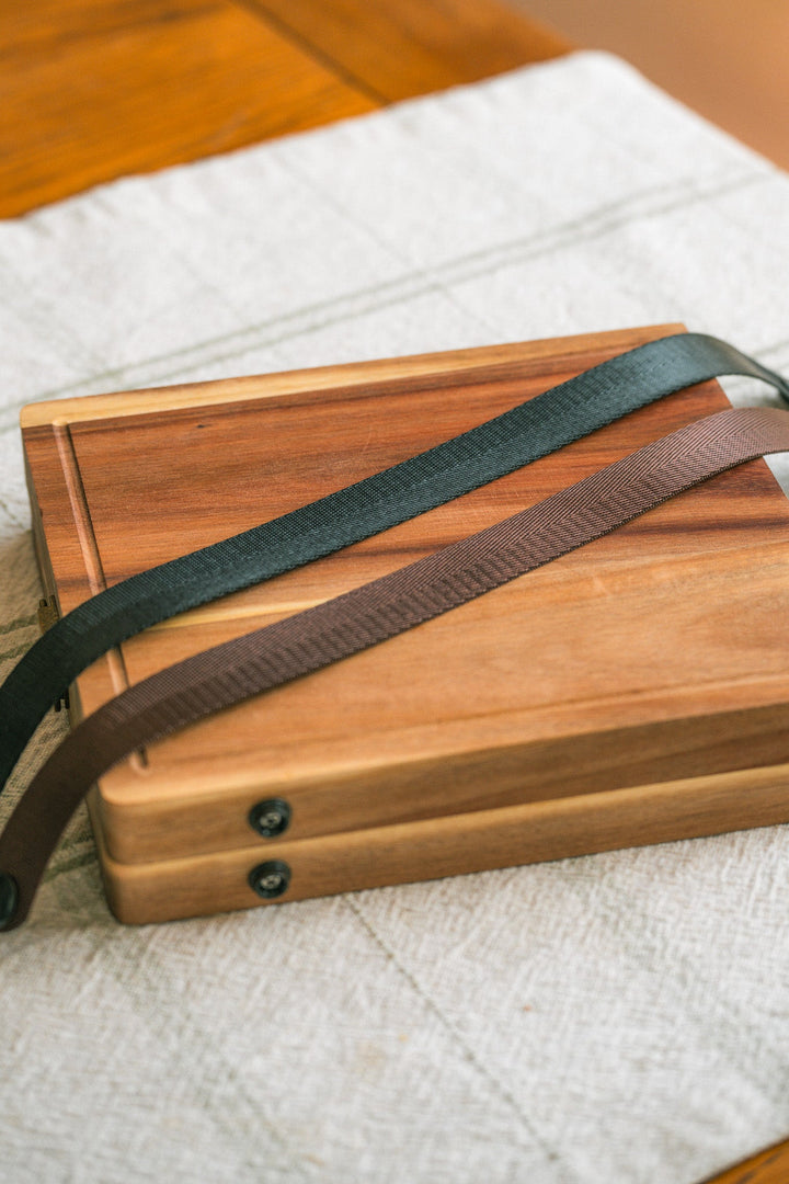 Folding wooden cheese board with dark green and brown webbing handles
