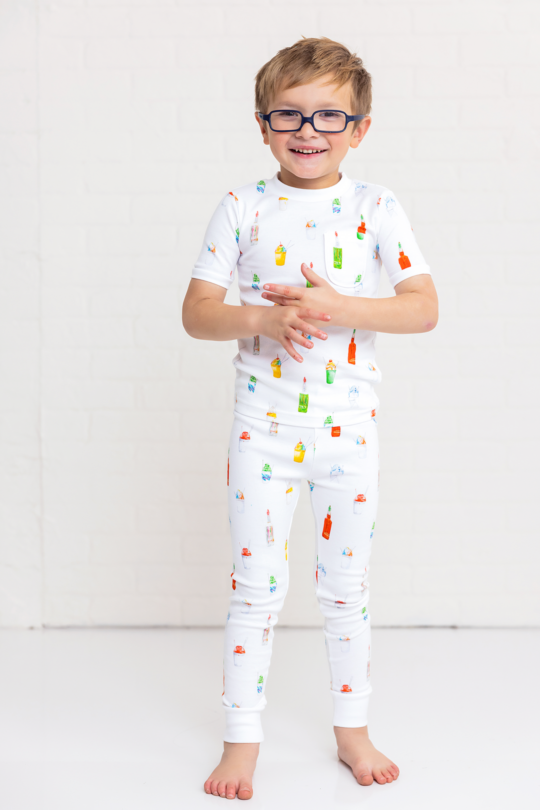 Child wearing white two-piece pajama set with colorful ice-pop pattern on shirt and pants